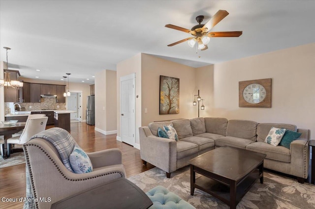 living room featuring dark wood-type flooring, ceiling fan with notable chandelier, and baseboards