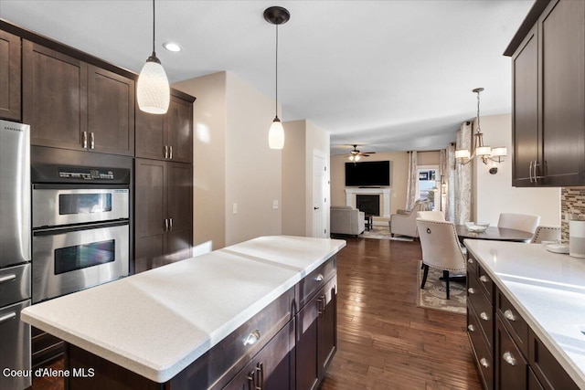 kitchen featuring dark brown cabinetry, open floor plan, dark wood finished floors, a fireplace, and stainless steel appliances