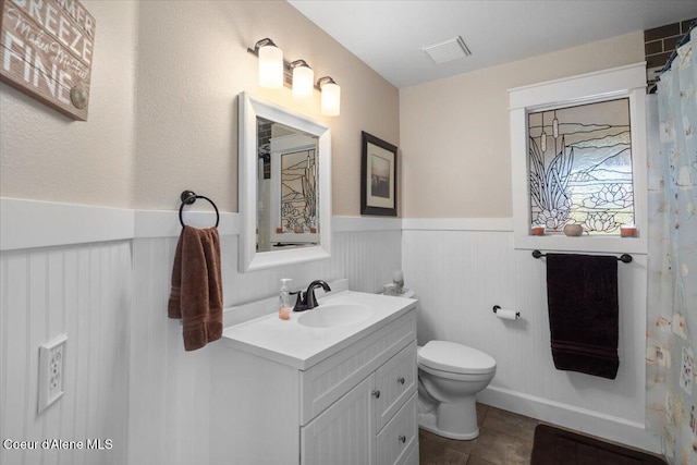 bathroom with vanity, visible vents, a wainscoted wall, tile patterned flooring, and toilet