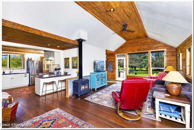 living room with ceiling fan, a wood stove, wood walls, dark wood-type flooring, and vaulted ceiling