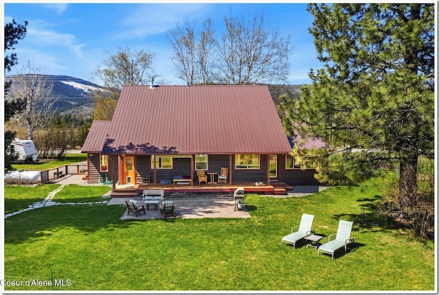 back of house with a deck with mountain view, a patio, a yard, and metal roof