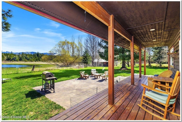 wooden deck with a lawn, fence, a patio area, and a water and mountain view