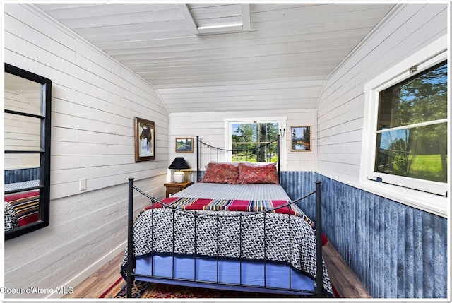 bedroom with wood walls, lofted ceiling, and wood finished floors