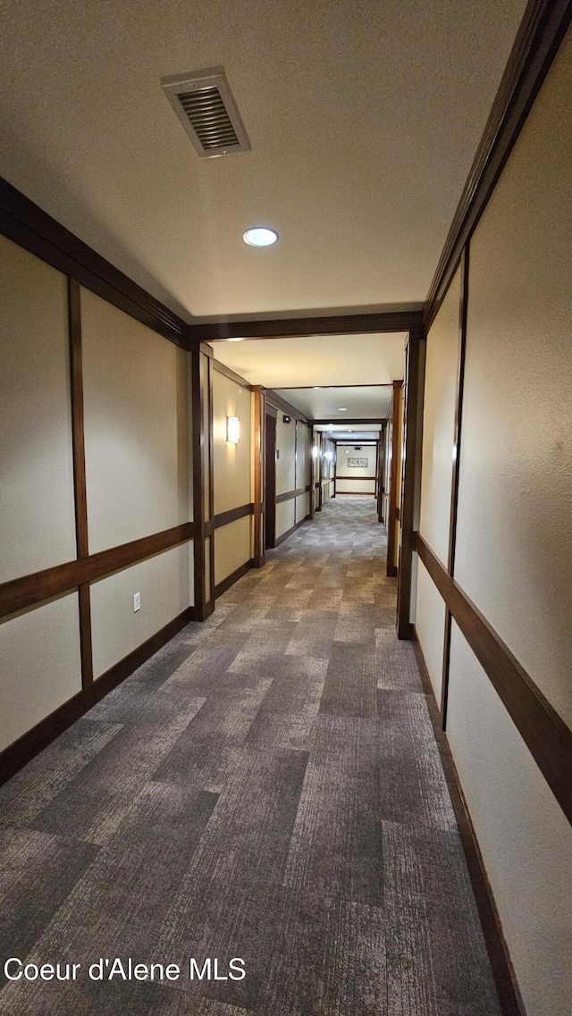 hallway with visible vents, baseboards, ornamental molding, and dark carpet