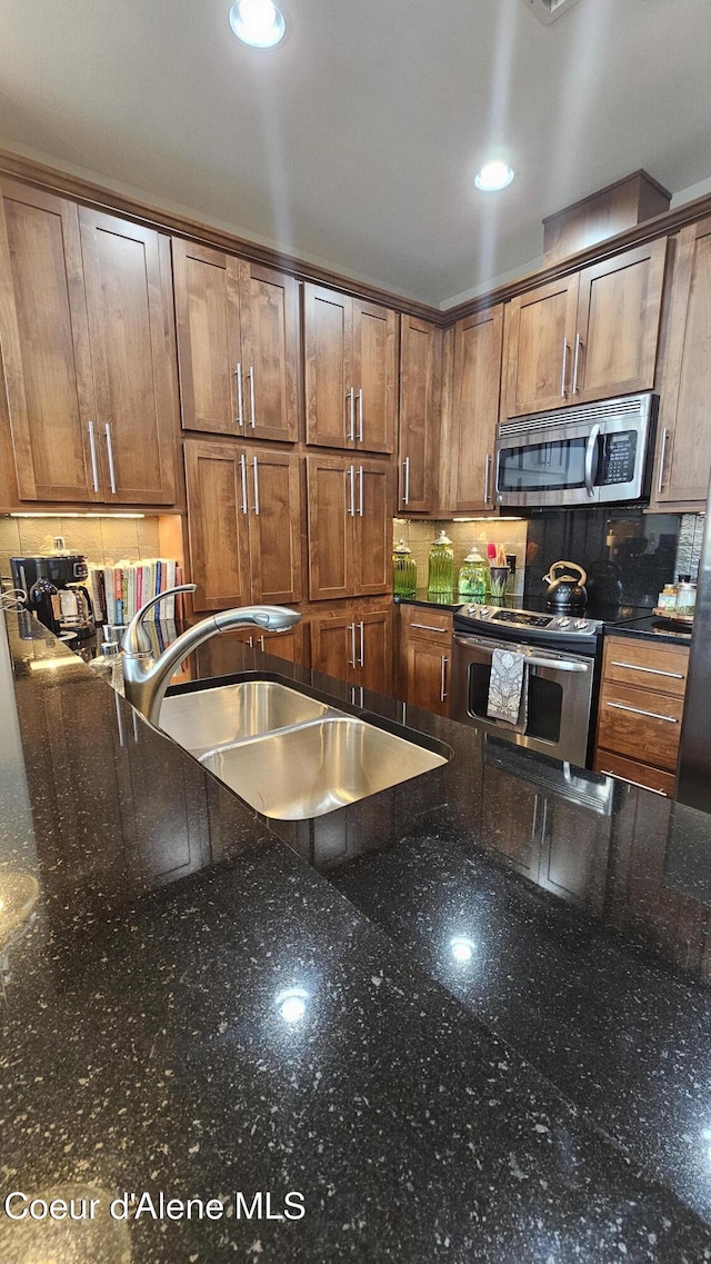 kitchen with dark stone counters, recessed lighting, a sink, appliances with stainless steel finishes, and backsplash