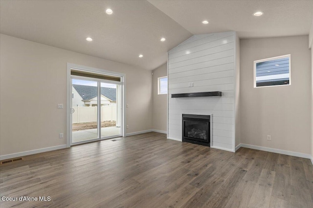 unfurnished living room with vaulted ceiling, wood finished floors, visible vents, and a large fireplace