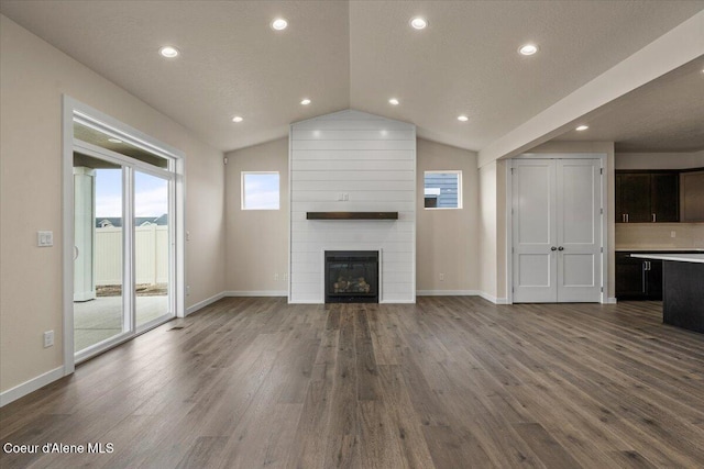 unfurnished living room with a large fireplace, baseboards, dark wood-type flooring, and lofted ceiling