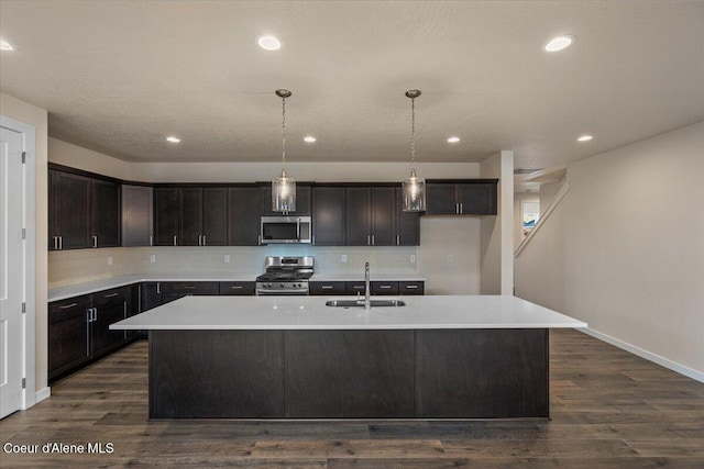 kitchen with a sink, stainless steel appliances, a kitchen island with sink, and dark wood-style flooring