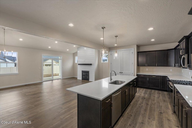 kitchen featuring dark wood-type flooring, a large fireplace, light countertops, stainless steel appliances, and a sink