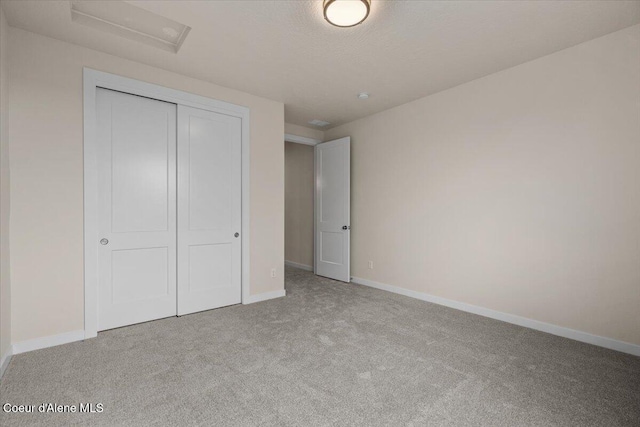 unfurnished bedroom featuring baseboards, a closet, carpet floors, and attic access