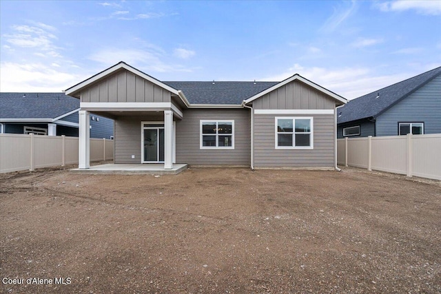 rear view of house featuring a shingled roof, board and batten siding, a fenced backyard, and a patio area