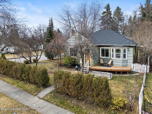 bungalow-style house with a wooden deck, roof with shingles, a front yard, and fence