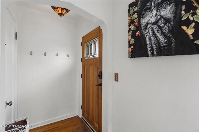 doorway featuring dark wood-style floors, arched walkways, and baseboards