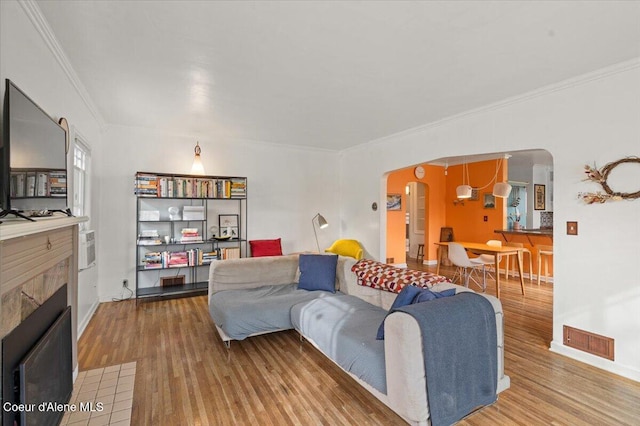 living room featuring visible vents, crown molding, a tile fireplace, wood finished floors, and arched walkways