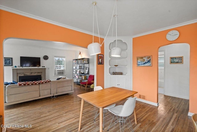 dining room with wood finished floors, visible vents, a fireplace, arched walkways, and ornamental molding