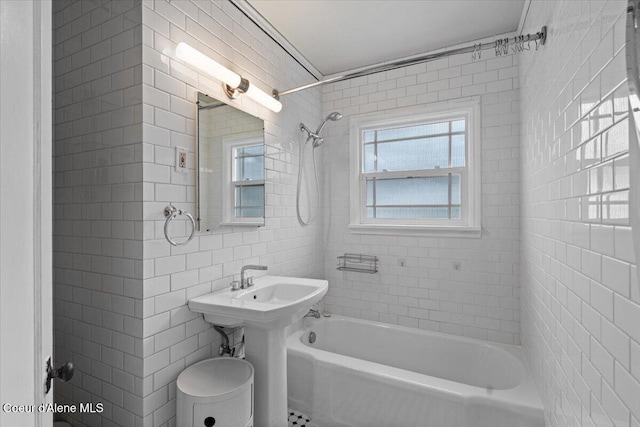 bathroom with a sink, tile walls, and washtub / shower combination