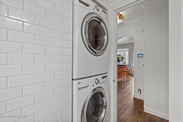 laundry room featuring stacked washer and clothes dryer, dark wood finished floors, arched walkways, crown molding, and laundry area