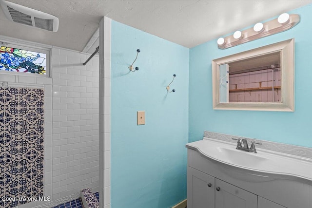 bathroom with vanity, visible vents, and a tile shower