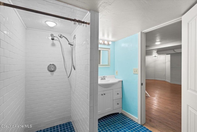 bathroom featuring vanity, baseboards, a tile shower, and a textured ceiling