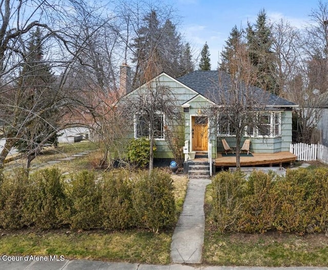 bungalow-style house featuring a deck, fence, roof with shingles, and a chimney