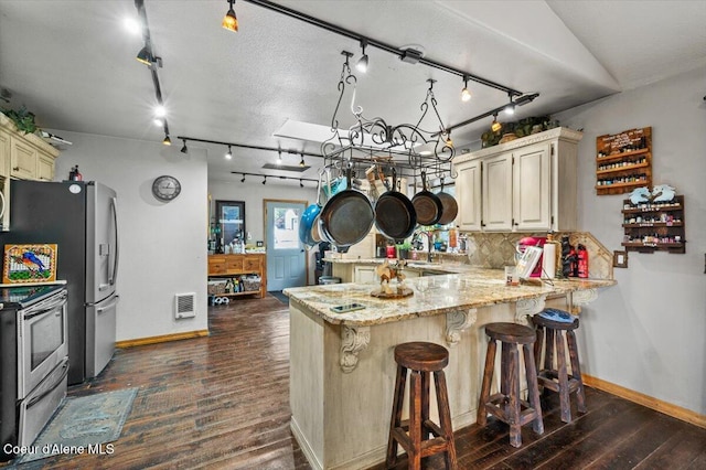 kitchen featuring stainless steel appliances, cream cabinetry, a peninsula, and dark wood-style flooring