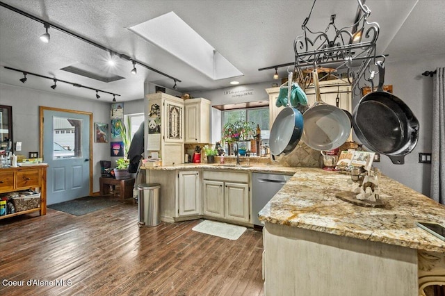 kitchen with dark wood finished floors, a skylight, cream cabinetry, a textured ceiling, and stainless steel dishwasher