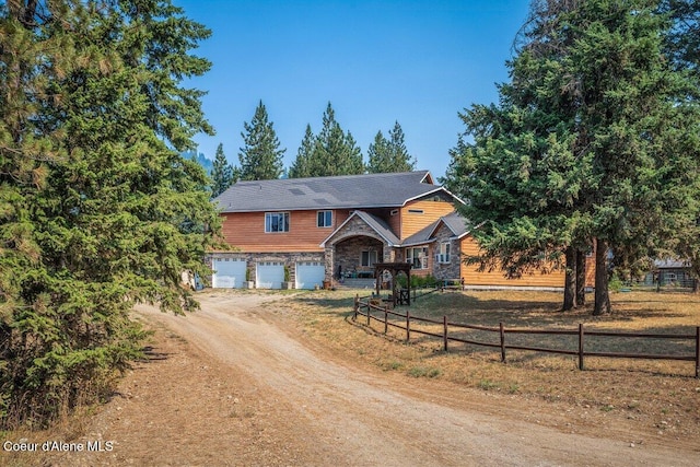 view of front of home with dirt driveway, stone siding, an attached garage, and fence