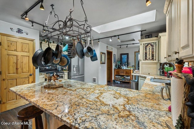 kitchen featuring light stone countertops, a skylight, stainless steel appliances, a sink, and cream cabinets