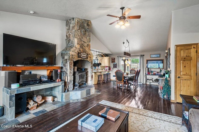 living area with hardwood / wood-style floors, lofted ceiling, a wood stove, ceiling fan, and a textured ceiling