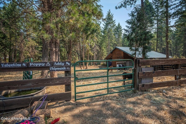 view of gate featuring an outbuilding, a forest view, and an exterior structure