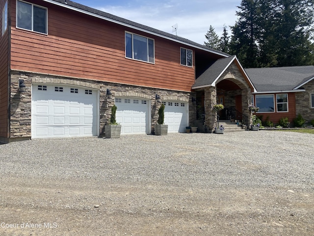 view of front facade with stone siding, gravel driveway, and a garage