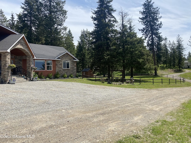 view of side of property featuring a yard, stone siding, a shingled roof, and fence