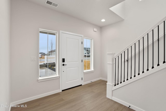 foyer entrance featuring visible vents, baseboards, wood finished floors, and stairway