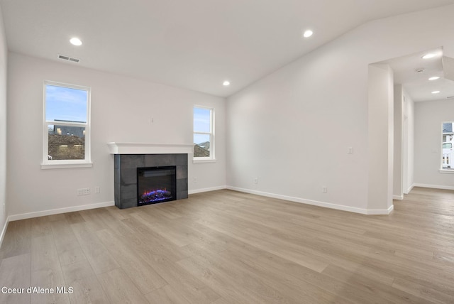 unfurnished living room with light wood-type flooring, visible vents, a tiled fireplace, recessed lighting, and lofted ceiling