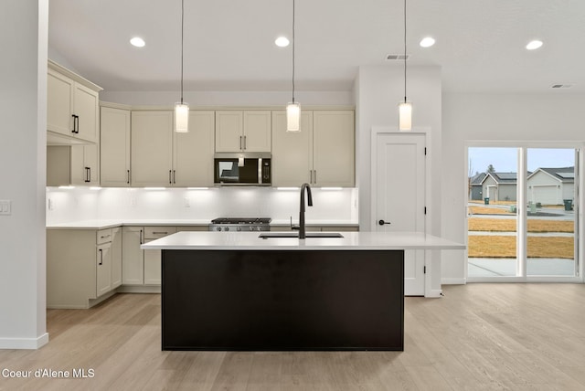 kitchen with stainless steel microwave, backsplash, visible vents, a center island with sink, and a sink