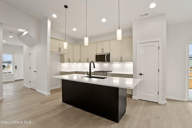 kitchen with stainless steel microwave, visible vents, light countertops, light wood-style floors, and a sink