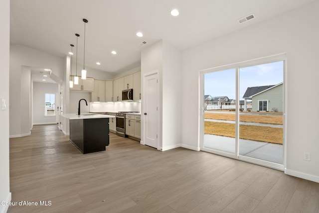 kitchen featuring visible vents, a kitchen island with sink, a sink, stainless steel appliances, and light wood finished floors