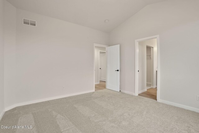 carpeted empty room with visible vents, baseboards, and vaulted ceiling