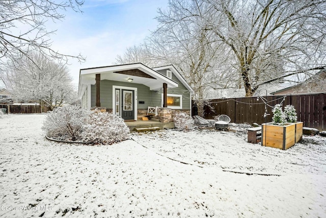 view of front of house with stone siding, covered porch, a vegetable garden, and fence