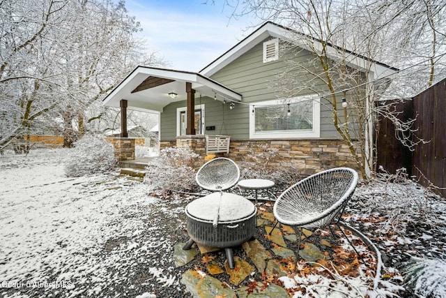 snow covered house featuring stone siding, a patio, and fence