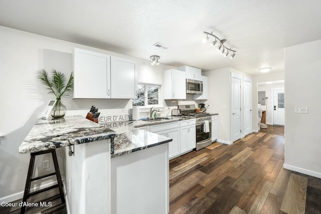 kitchen with dark wood-type flooring, a peninsula, stone countertops, stainless steel appliances, and a sink