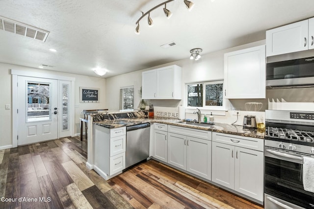 kitchen with visible vents, appliances with stainless steel finishes, a peninsula, white cabinets, and a sink