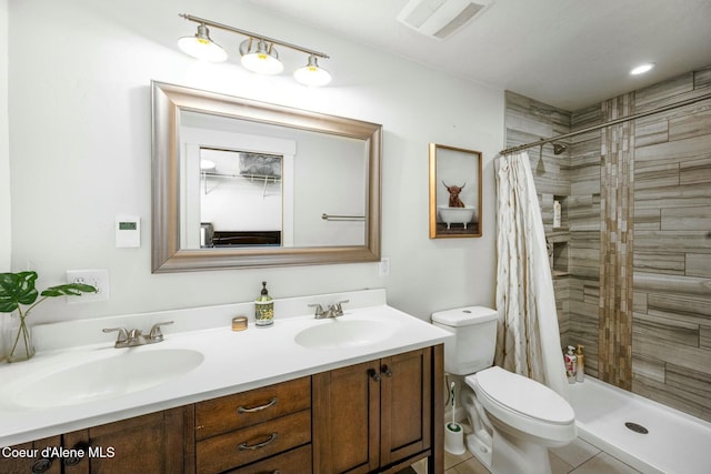 bathroom with double vanity, toilet, tiled shower, and a sink