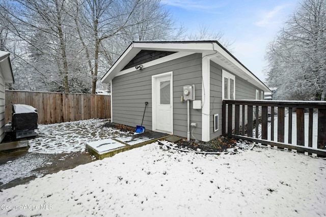 snow covered structure featuring an outdoor structure and fence