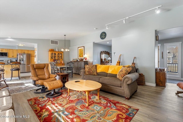 living room with light wood finished floors, visible vents, baseboards, rail lighting, and a notable chandelier