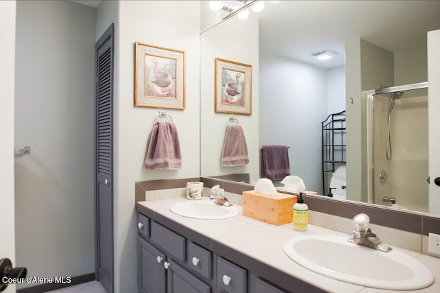 bathroom with double vanity, toilet, a shower with shower door, and a sink