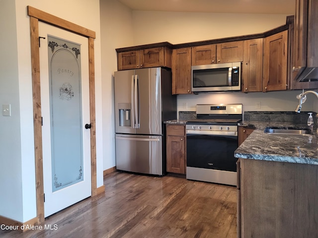 kitchen featuring dark stone counters, lofted ceiling, appliances with stainless steel finishes, dark wood-style floors, and a sink