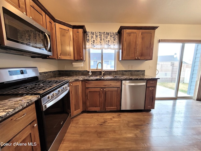 kitchen with a sink, appliances with stainless steel finishes, dark stone countertops, and a healthy amount of sunlight