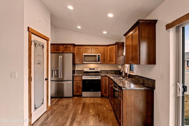 kitchen with dark stone countertops, recessed lighting, a sink, stainless steel appliances, and vaulted ceiling