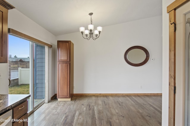 unfurnished dining area with an inviting chandelier, light wood-style floors, baseboards, and lofted ceiling